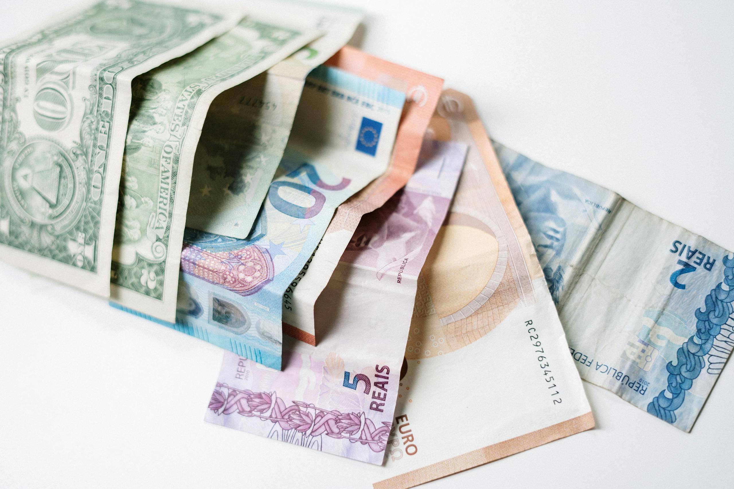 Resources A collection of different international currency notes, including US Dollar, Euro, and Brazilian Real, on a white background.